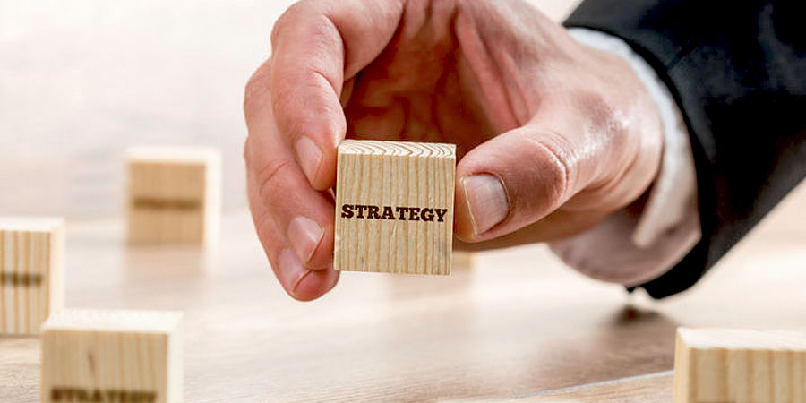 Male hand holding a small block with the words "Strategy" on it.