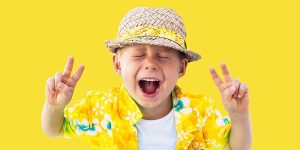A boy giving the peace sign in a yellow Hawaiian shirt with yellow background.