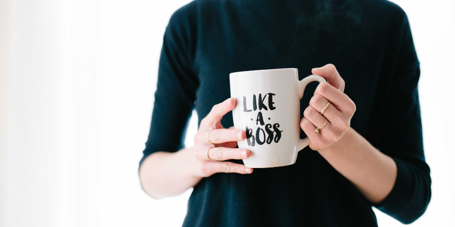 Woman in a long sleeved dark green shirt holding a white mug that says "like a boss" in black lettering.