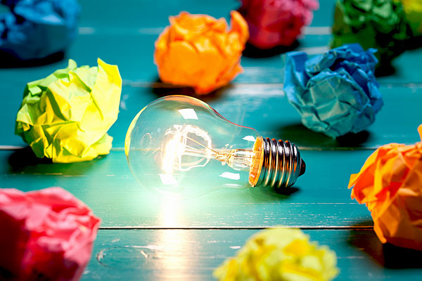 Single lightbulb shining with crumpled colored paper all around it.