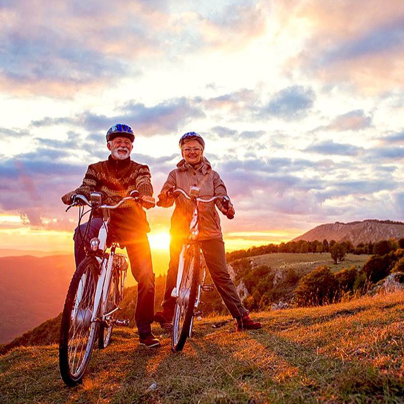 Senior couple riding their bikes across grassy plain at sunrise.