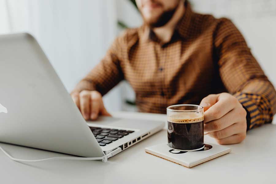 Man working on a laptop computer holding a cup of coffee